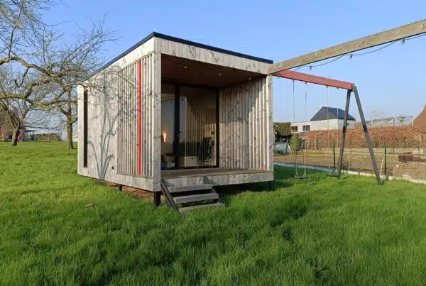 Moderne houten buitenruimte met schommel en grote ramen, gelegen in een groene tuin. Voorbeeld van duurzame speel- en leeromgevingen.